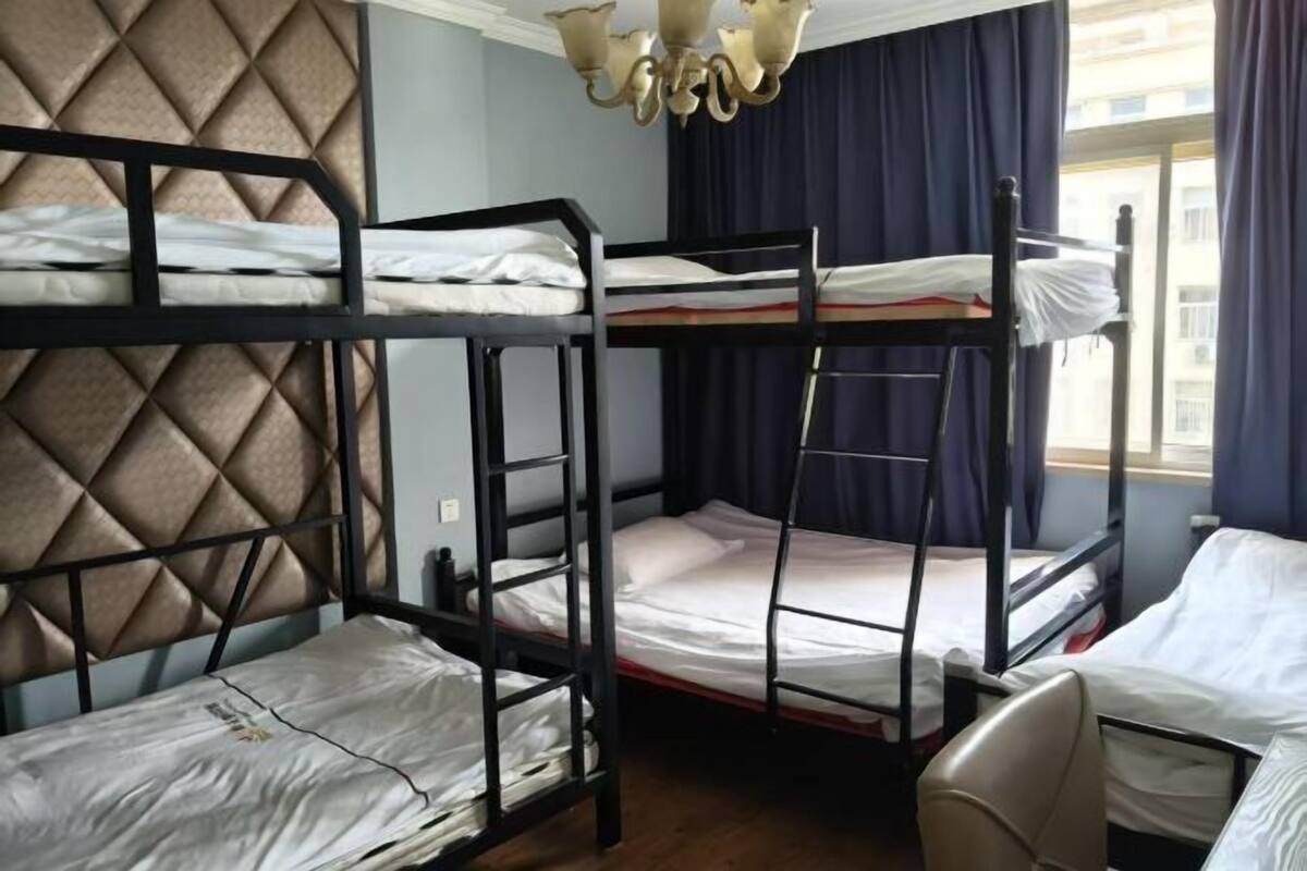 Une chambre avec un lit superposé, un lustre, une fenêtre avec des rideaux et un mur orné d’un motif géométrique.
