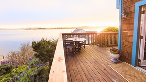 A wooden deck with a table and chairs, overlooking a calm lake with a distant shoreline. - Romantic Waterfront/Fire Pit/Hot Tub/Mins. to Beaches & Restaurants/Pet Friendly (Bodega Bay)