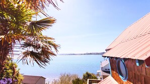 A coastal view with a wooden building featuring a large circular window, overlooking a calm body of water and distant land. - Romantic Waterfront/Fire Pit/Hot Tub/Mins. to Beaches & Restaurants/Pet Friendly (Bodega Bay)