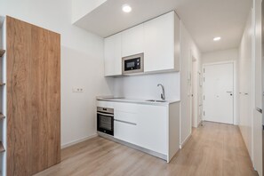 Cozinha compacta com armários brancos, micro-ondas, forno e pia.