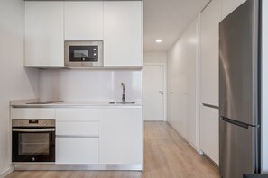 Une cuisine moderne avec des meubles blancs, un four encastré, un four à micro-ondes et un réfrigérateur en acier inoxydable.