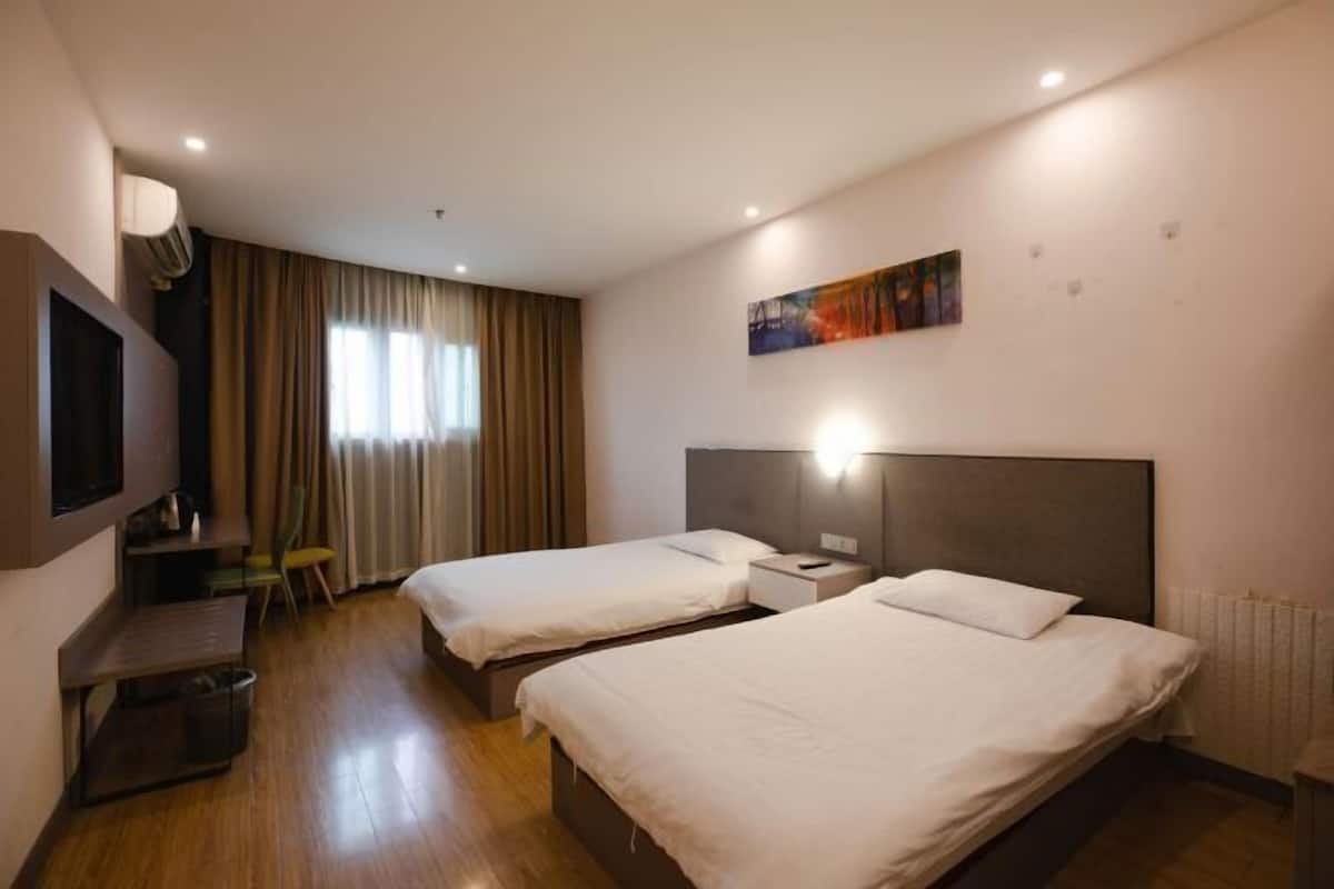 A hotel room with two beds, a TV, a desk, and a painting on the wall.