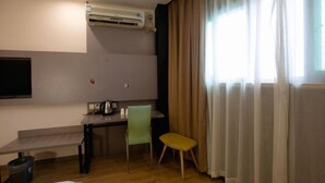 Habitación de hotel con cama, escritorio, silla, televisor y aire acondicionado.