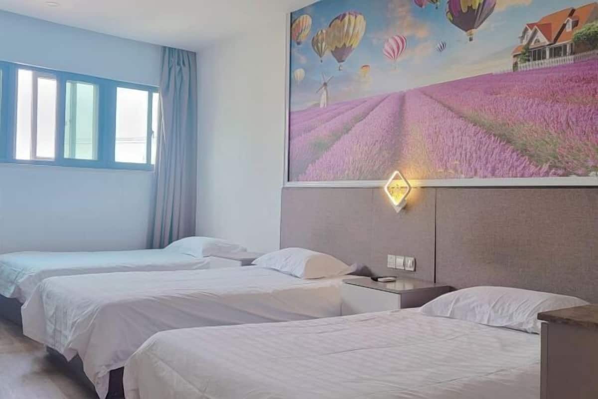 A hotel room with two beds, a window with curtains, and a mural of hot air balloons and a windmill.