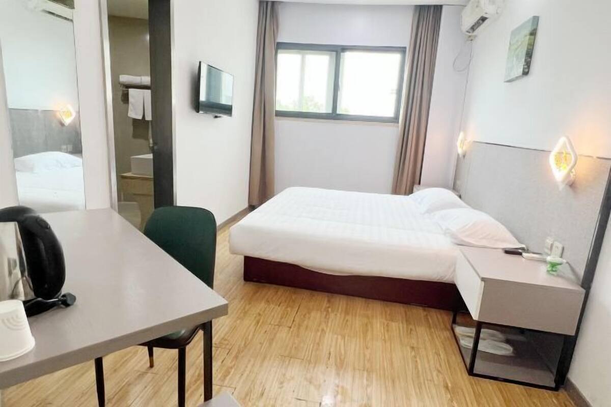 A hotel room with a bed, a desk, a chair, a TV, and a window with curtains.