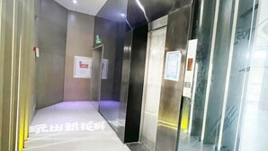 Un área de ascensor moderna con paredes metálicas y puertas de vidrio, que incluye señalización de salida de emergencia y un piso de baldosas impecables.