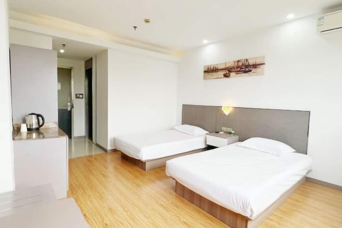A modern hotel room with two single beds, a small desk with a kettle, and a painting on the wall.