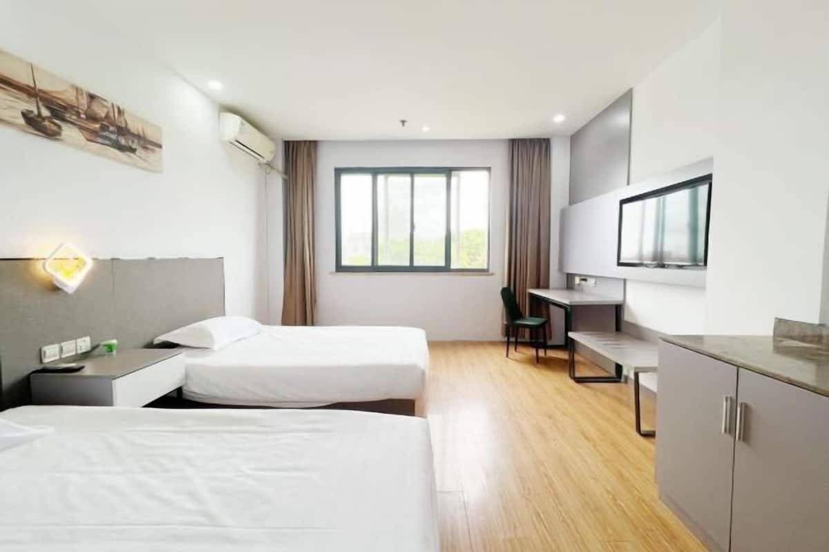 A hotel room with two beds, a desk, a chair, a TV, and a window.