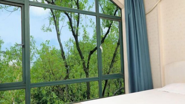 A room with a bed, a window with a view of trees, and a curtain. - Fuman Hostel (Shanghai)
