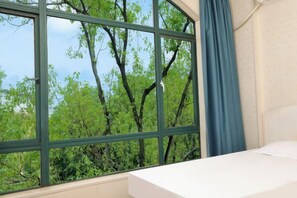 A room with a bed, a window with a view of trees, and a curtain. - Fuman Hostel (Shanghai)