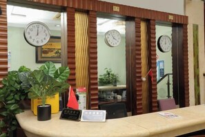 Un comptoir d’accueil avec des horloges, une plante en pot et un panneau.