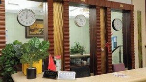 A reception area with a counter, potted plants, and clocks on the wall. - Fuman Hostel (Shanghai)