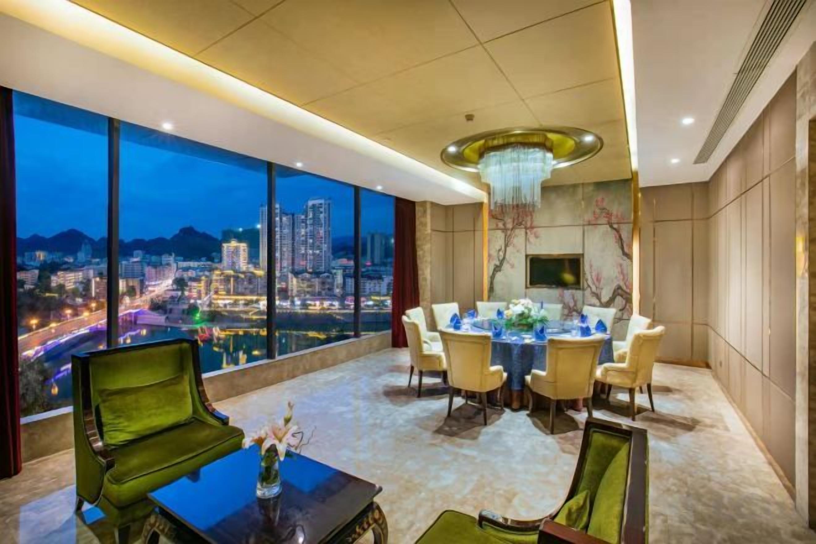 Habitación de hotel en un rascacielos con vistas panorámicas de la ciudad, un área de comedor con una mesa redonda y un candelabro.