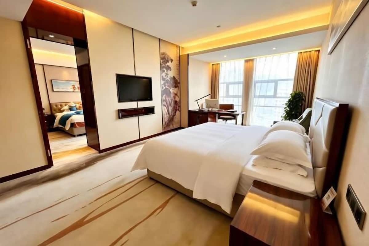 Una habitación de hotel moderna con una cama grande, un escritorio, un televisor de pantalla plana y un amplio ventanal con cortinas.