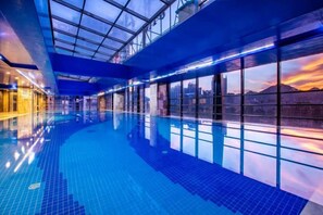 Una piscina interior con techo de vidrio, ventanas amplias y vistas a la ciudad.