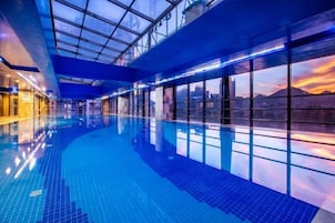 Una piscina interior con techo de vidrio, ventanas amplias y vistas a la ciudad.