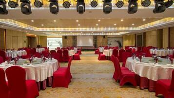 A banquet hall with round tables, red chairs, and a carpeted floor.
