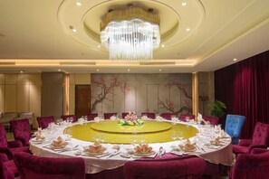 Un salón de conferencias con una mesa redonda, sillas rojas y una araña de cristal.