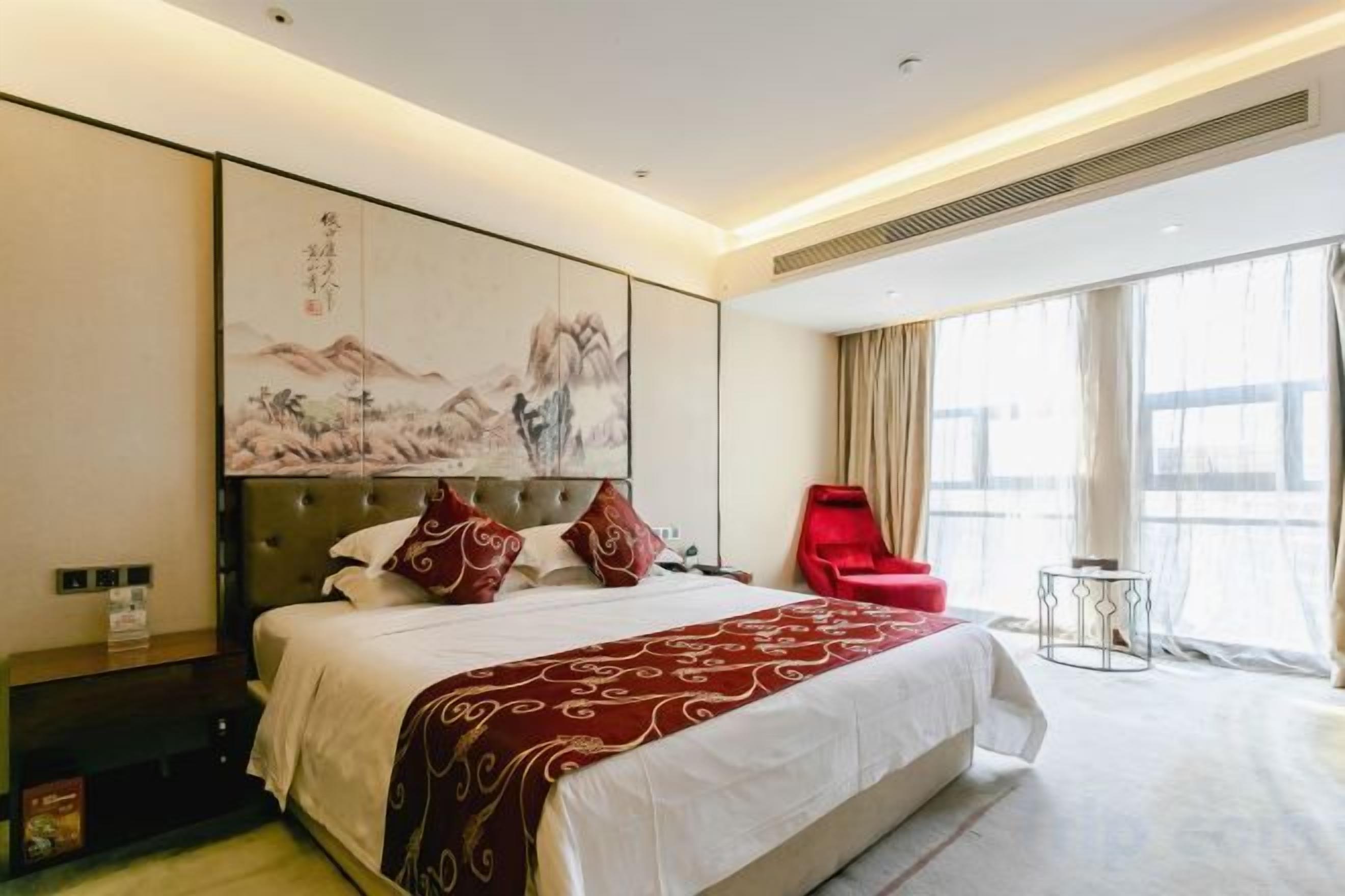 Habitación de hotel con una cama grande, una silla roja y vistas al exterior.