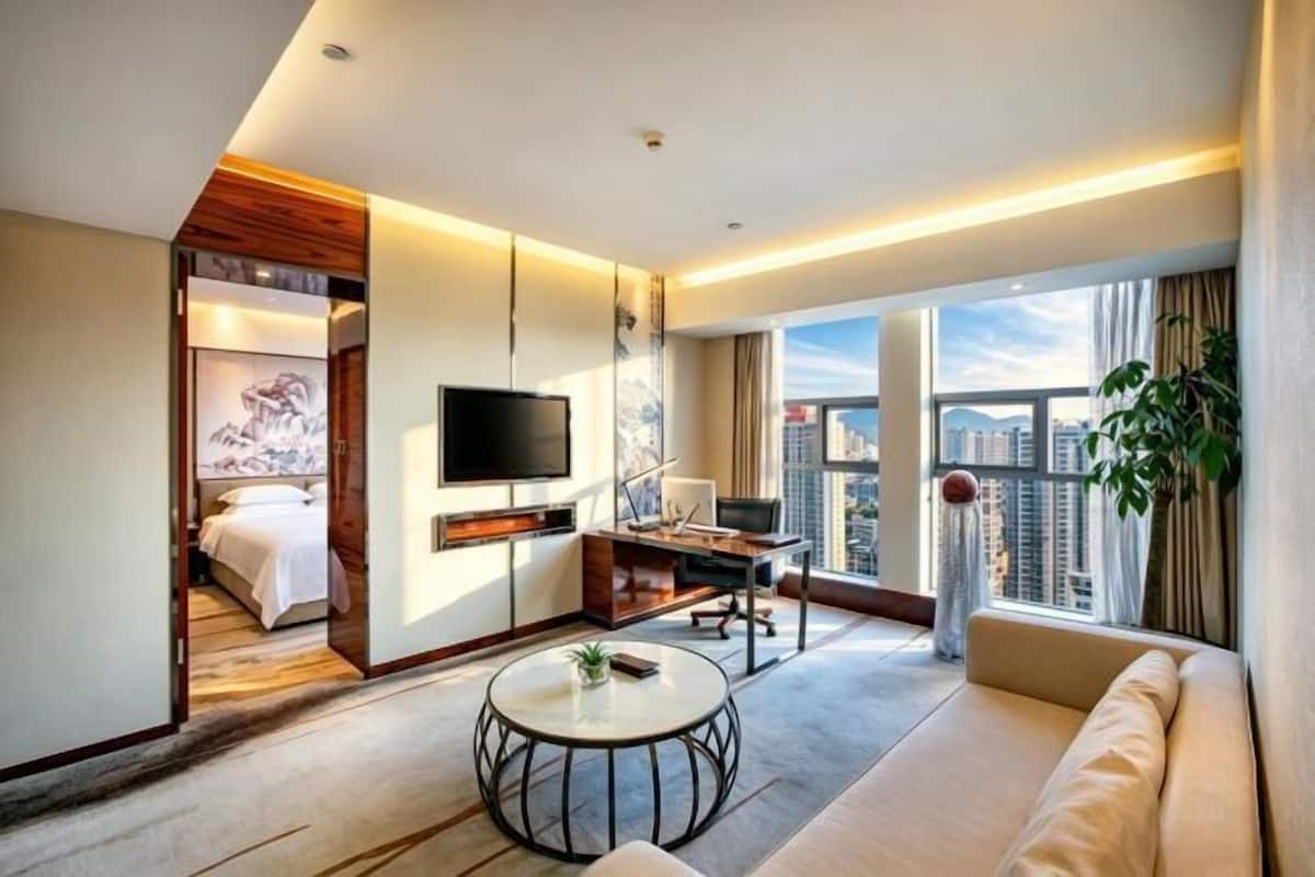 Una habitación de hotel moderna con cama, TV, escritorio, sofá y un amplio ventanal con vistas a la ciudad.