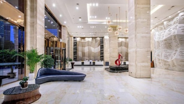 A spacious lobby with a curved blue sofa, a wooden coffee table, and a red sculpture. - Tongren Jinjiang Hotel (Tongren)