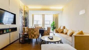 A hotel room with a flat-screen TV, a sofa, a dining table with chairs, and a small round table.