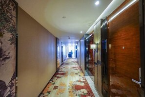 Un pasillo de hotel con alfombra floral, puertas de madera y una persona a lo lejos.