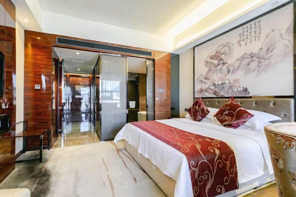 Una habitación de hotel moderna con una cama grande, un escritorio de madera y una puerta corredera de vidrio que da a un baño.