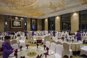 A banquet hall with round tables, white chairs, and staff in uniform. - Tongren Jinjiang Hotel (Tongren)