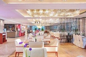 Un vestíbulo de hotel con mostrador de recepción, zona de estar y una lámpara decorativa.