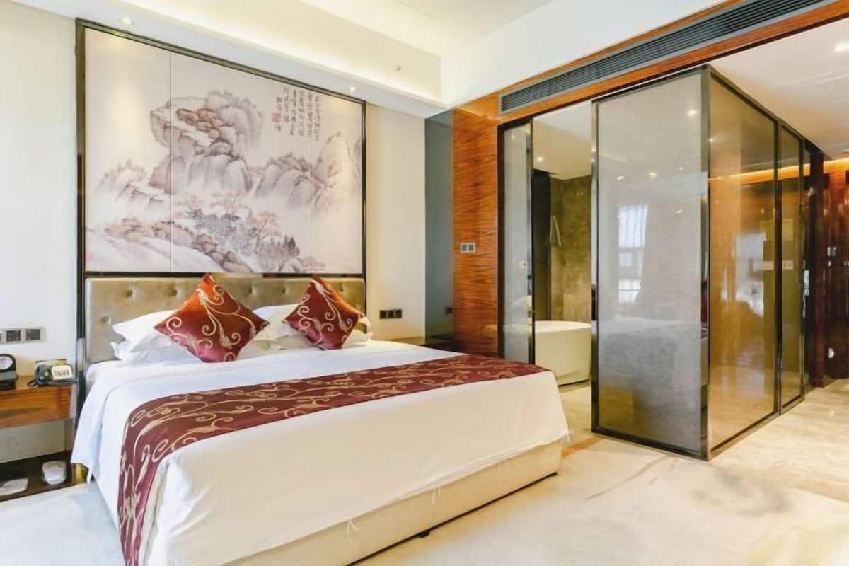Habitación de hotel moderna con una cama grande, una obra de arte colgada en la pared y una puerta corredera de vidrio que da al baño.