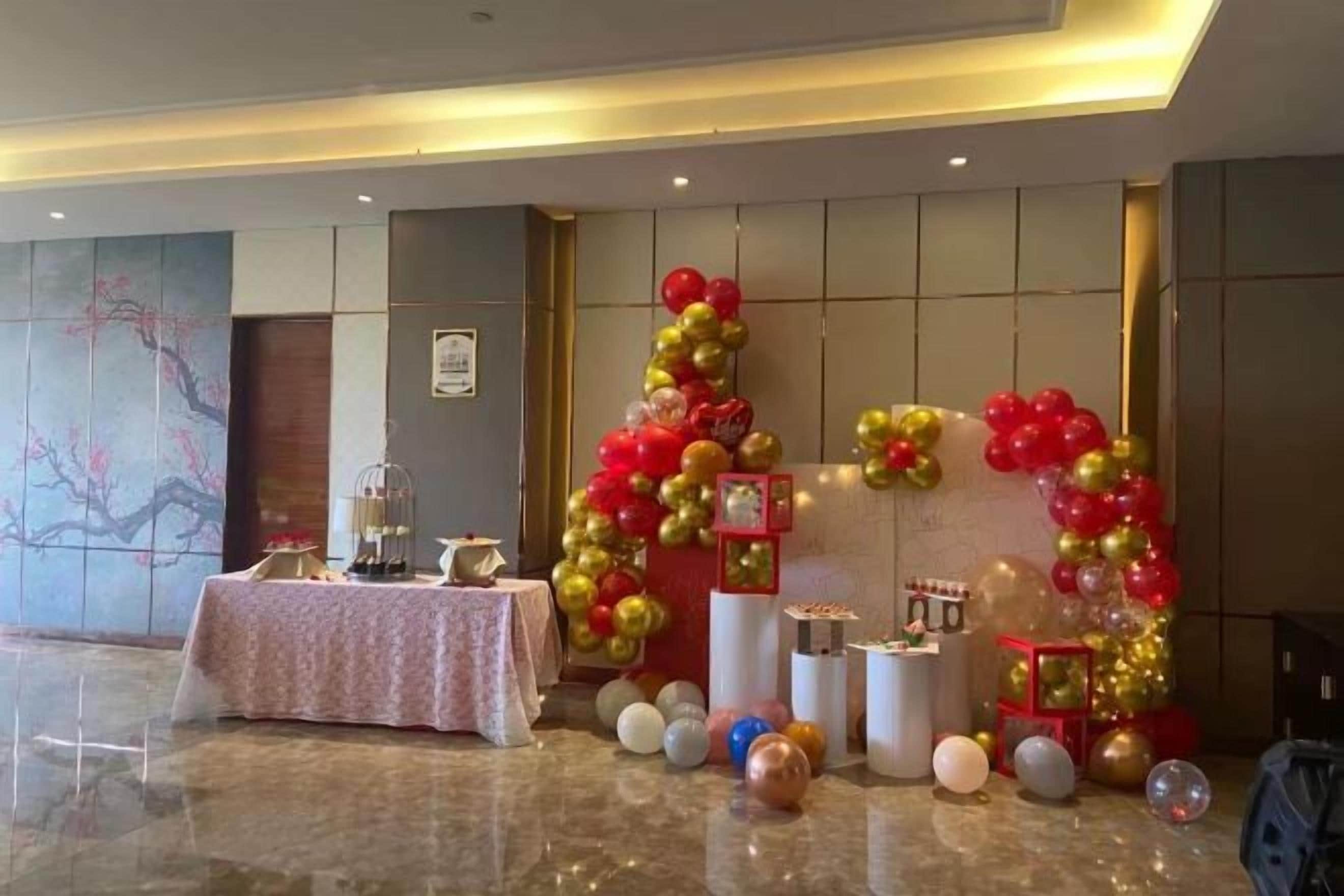 Un espace événementiel décoré avec une table, des ballons et un mur orné d’un tableau encadré.