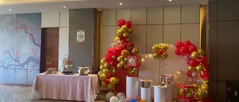 Un espace événementiel décoré avec une table, des ballons et un mur orné d’un tableau encadré.