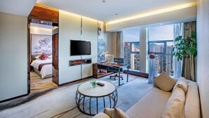 A modern hotel room with a large bed, a TV, a desk, and a sofa. There is a view of a cityscape through large windows. - Tongren Jinjiang Hotel (Tongren)