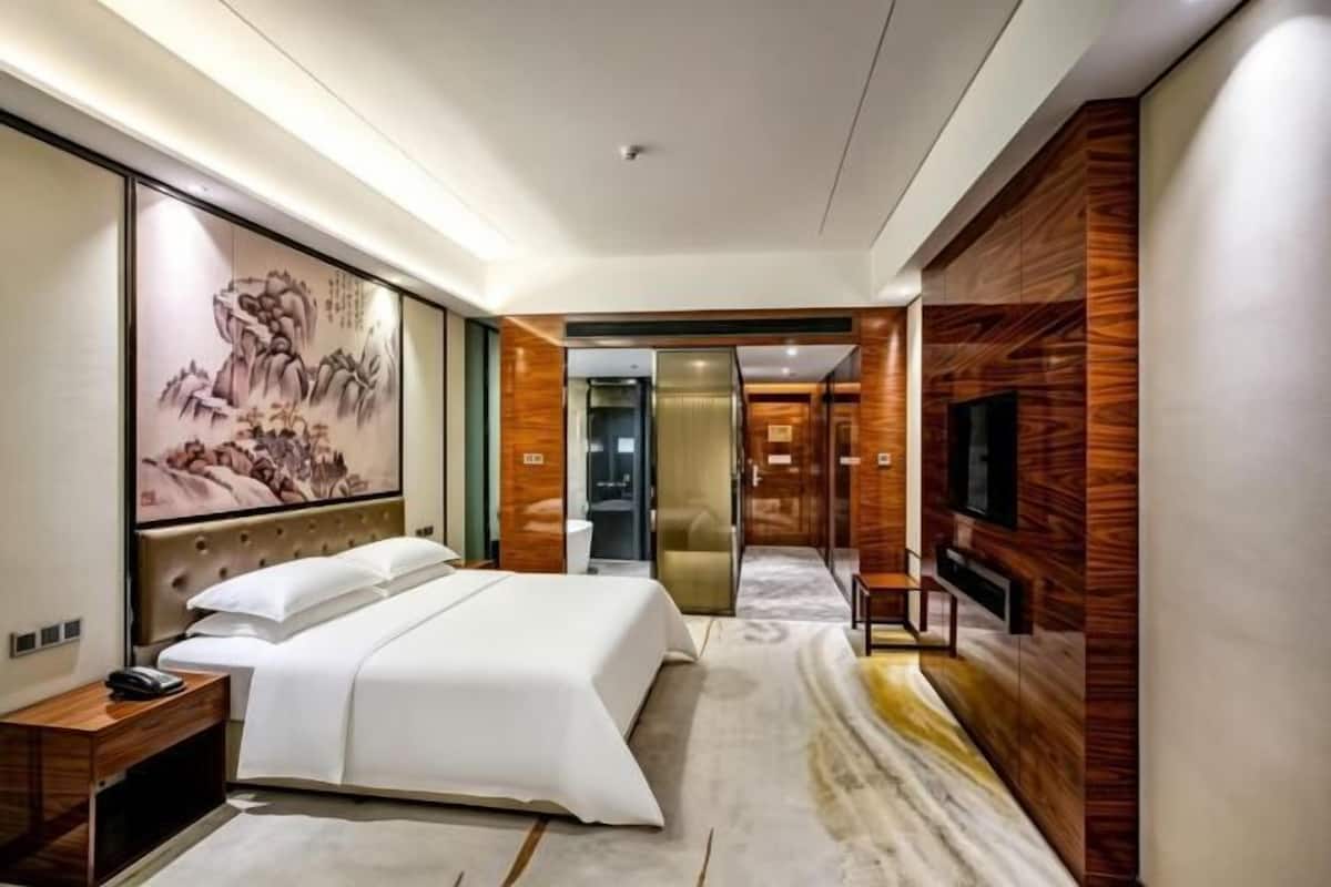 Una habitación de hotel moderna con una cama grande, un televisor de pantalla plana, un panel de madera decorativo y una obra de arte de gran tamaño en la pared.