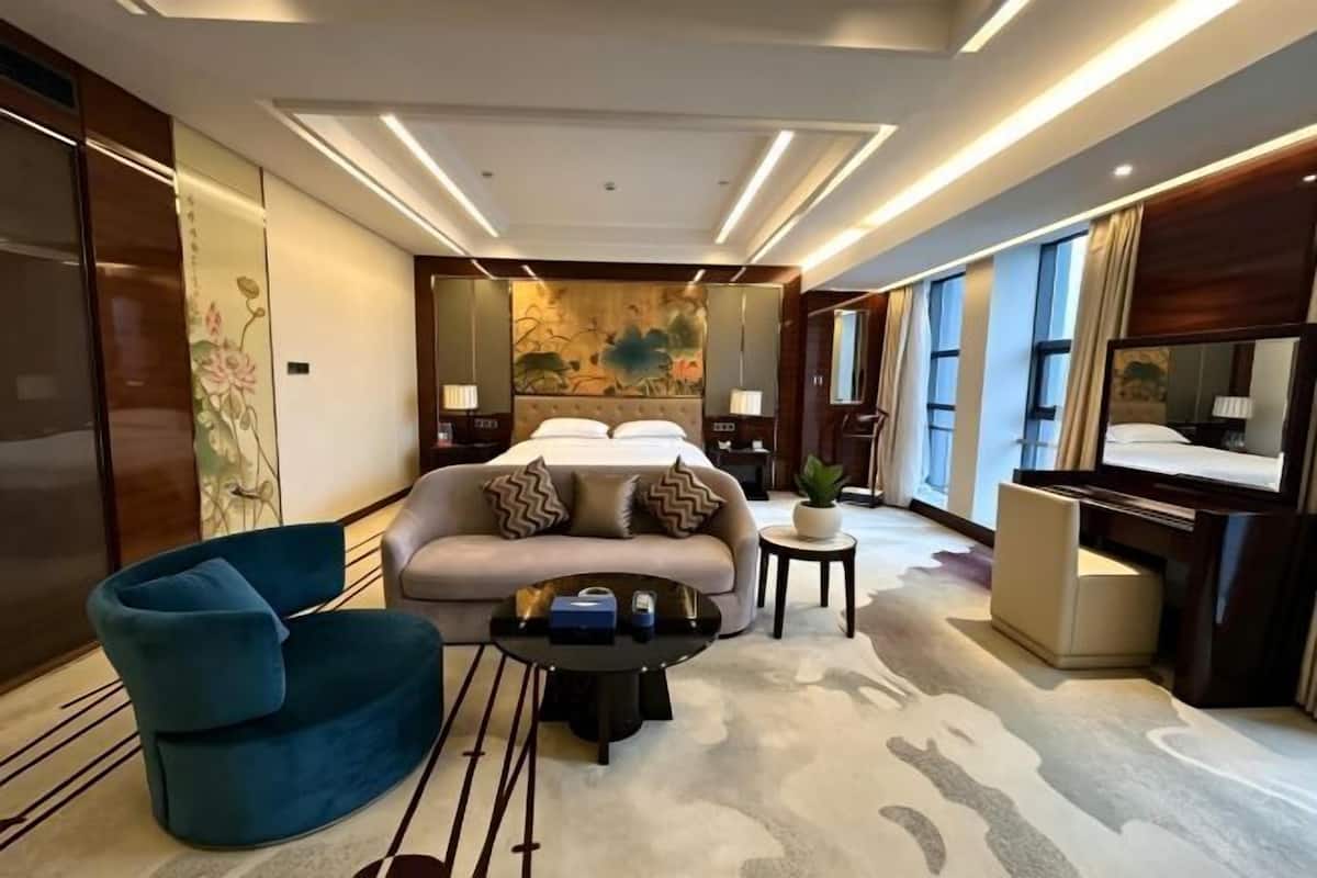 Una habitación de hotel moderna con un sofá, una silla, una cama, una mesita y un piano.