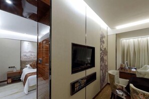 A hotel room with a bed, a television, a seating area, and a mirror. - Tongren Jinjiang Hotel (Tongren)
