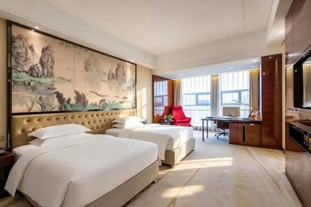Habitación de hotel con dos camas, un escritorio, una silla y un cuadro grande en la pared.