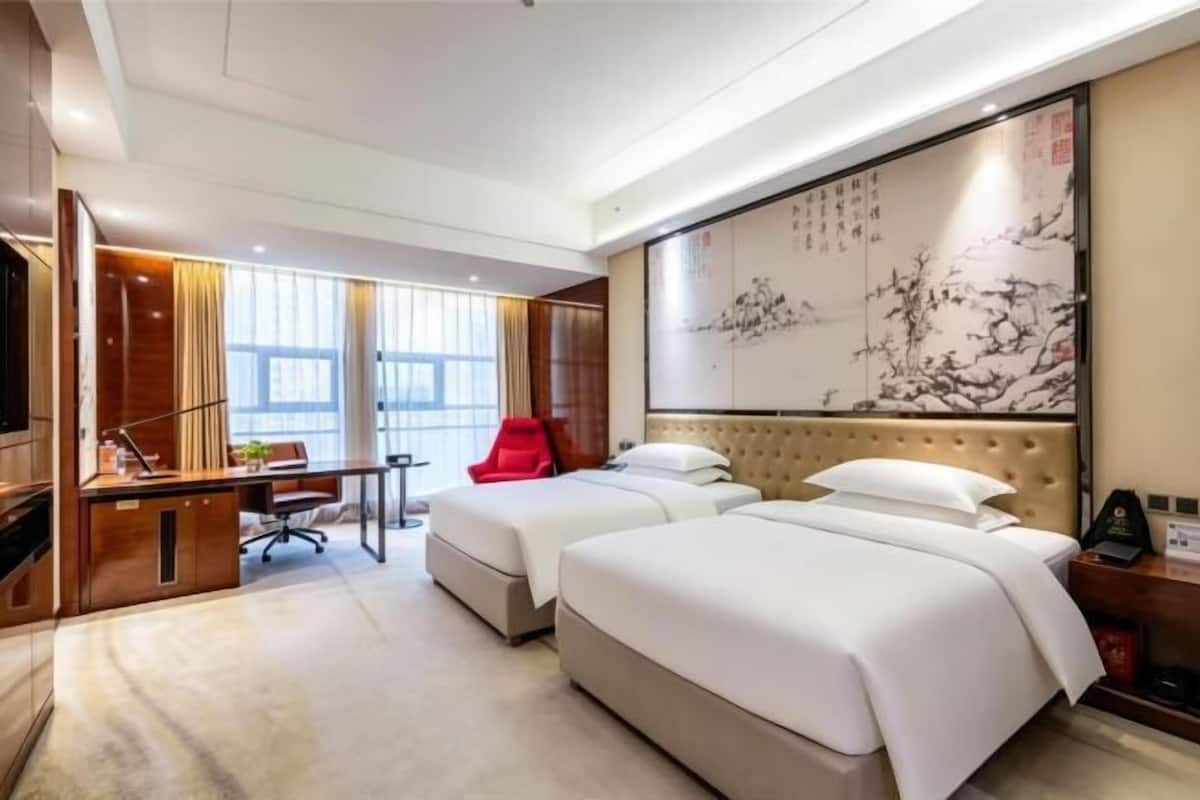 Habitación de hotel con dos camas, un escritorio con silla, un televisor y un cuadro grande en la pared.