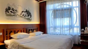 Une chambre d’hôtel avec un lit, un tableau accroché au mur, une grande fenêtre avec des rideaux et une tête de lit en bois.