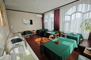Quarto de hotel com área de jantar, televisão e uma grande janela com cortinas.