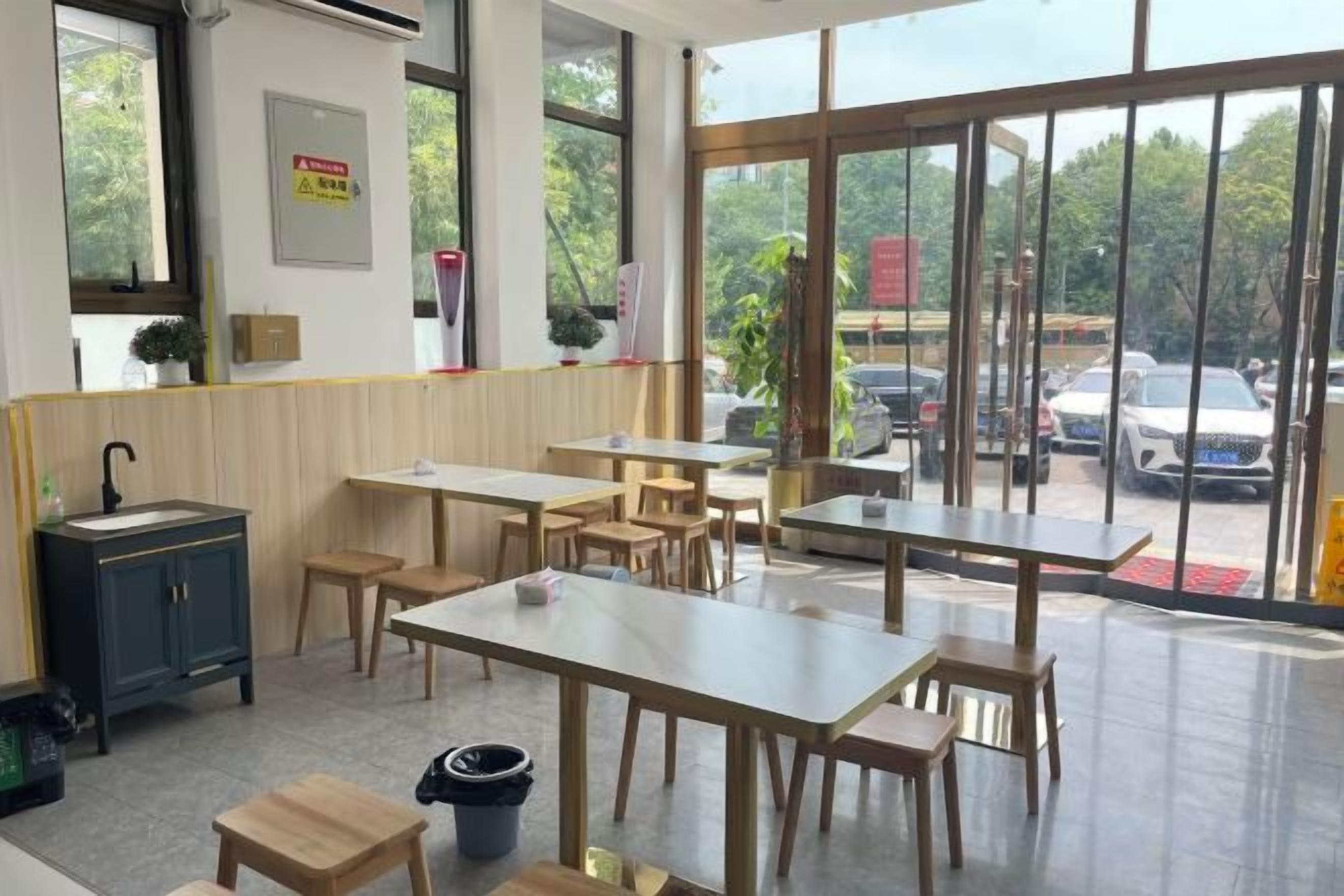 A restaurant interior with tables and chairs, a sink, and large windows.