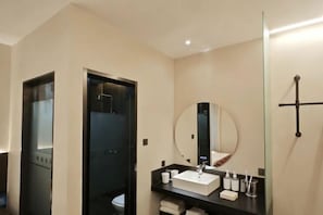 A modern bathroom with a glass shower enclosure, a round mirror, and a black countertop with a white sink.