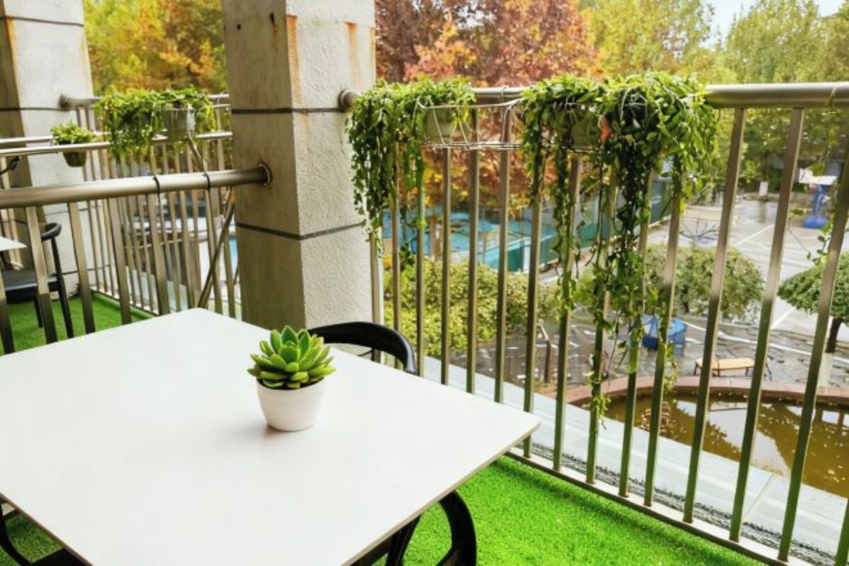 A balcony with a white table, a potted plant, and green plants hanging on the railing.