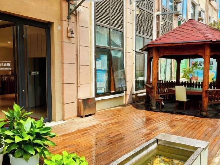 A wooden deck with a gazebo, potted plants, and a building entrance.