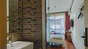 A modern hotel room with a brick accent wall, a large window with curtains, a bed, a bedside table, and a TV mounted on the wall. - The XJ Hotel (Beijing)