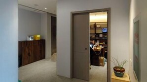 A hallway with a wooden cabinet, a door leading to a room with a television, and a potted plant. - The XJ Hotel (Beijing)