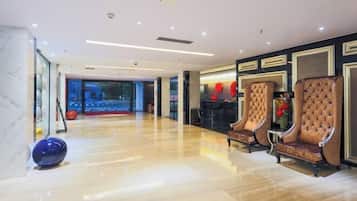 A spacious lobby with a polished wooden floor, two tufted armchairs, and a glass partition with a view of the outside.