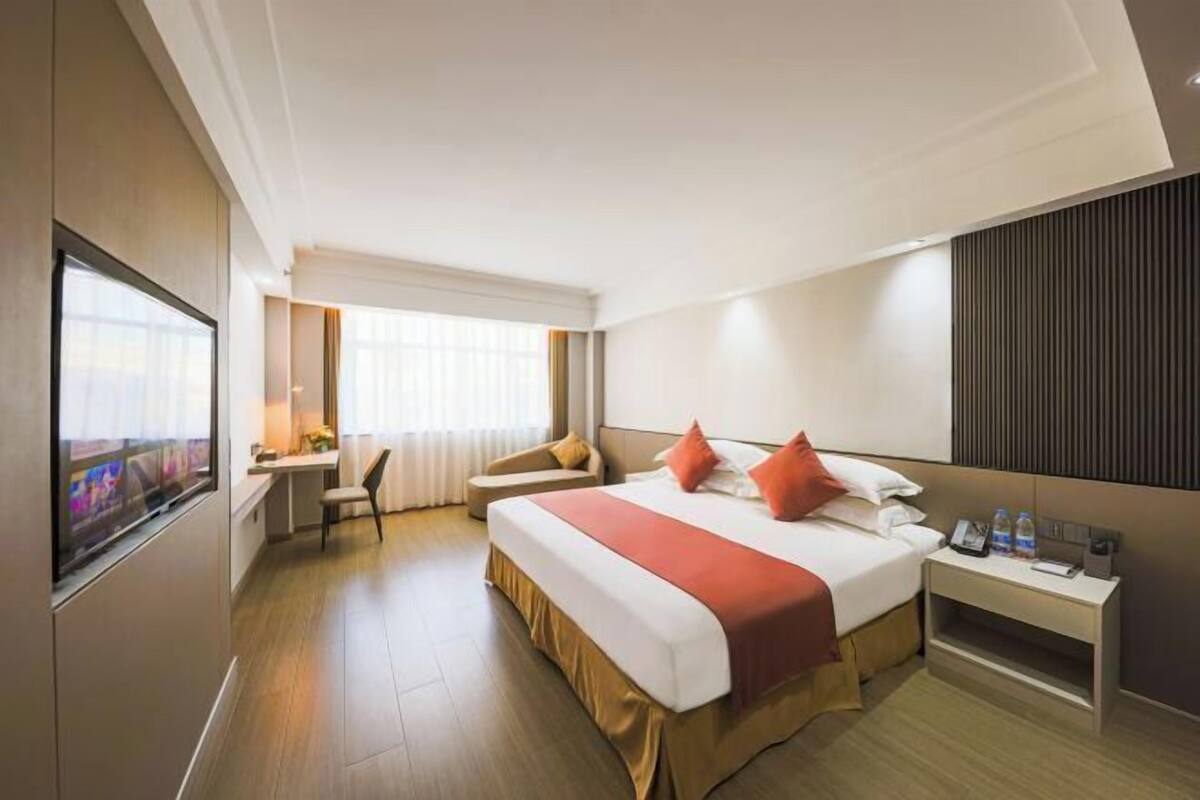 A hotel room with a large bed, a desk, and a TV.