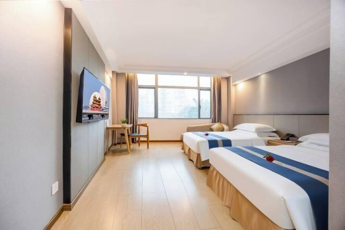 A hotel room with two beds, a TV, a desk, and a window.